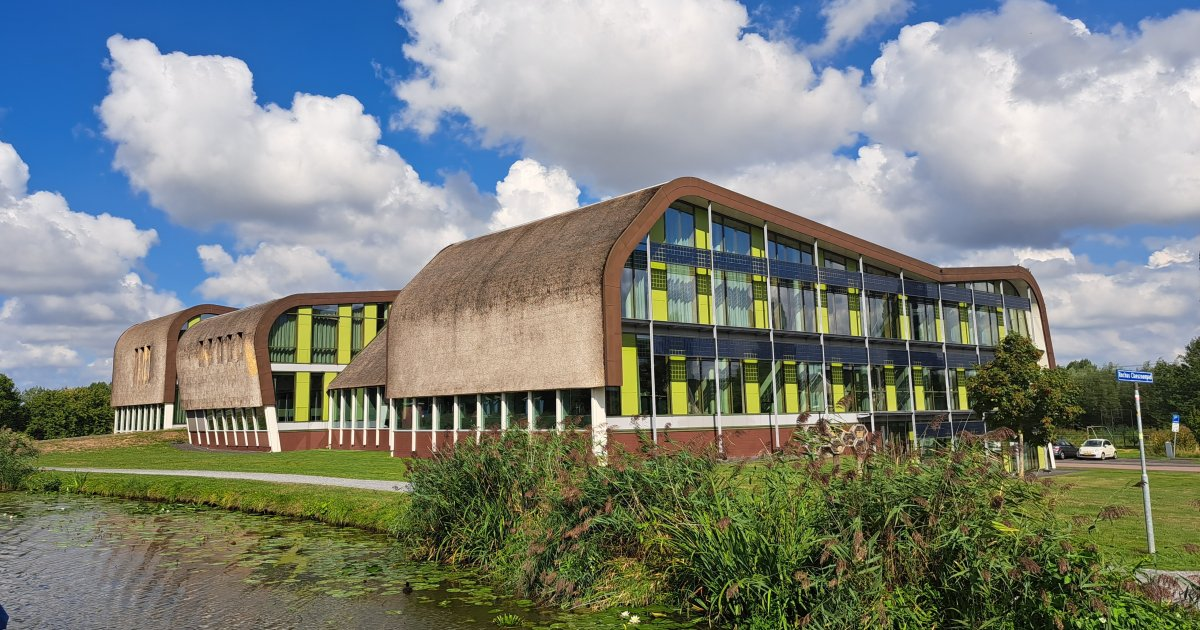 Het gemeentehuis van Midden-Delfland in Schipluiden, met een rieten dak, groene gevel en water op de voorgrond